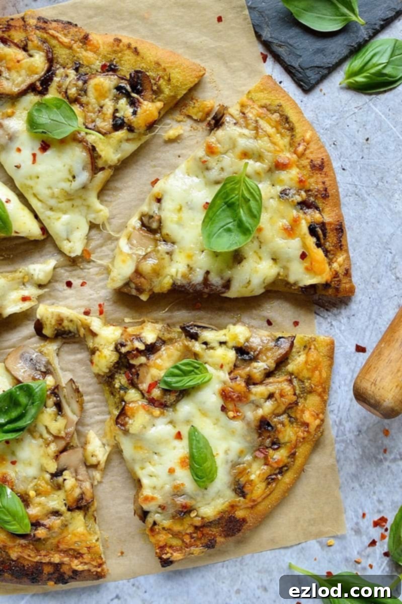 Earthy Pesto Mushroom Pizza 4 A slice of mushroom pesto pizza being lifted from the whole pizza, showcasing the melted cheese and a vibrant pesto base.