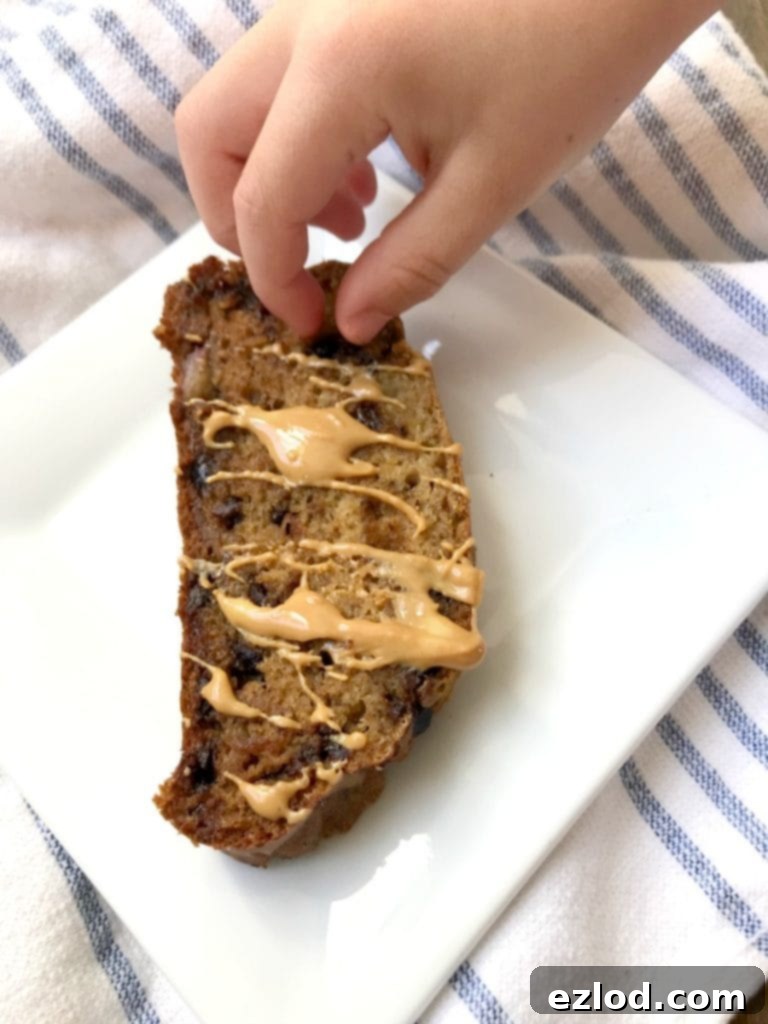 Overhead photo of a child's hand sneaking a chocolate chip from a slice of gluten free banana bread drizzled with melted peanut butter.