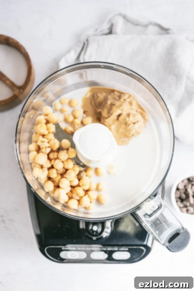 Chickpeas and nut butter being blended in a food processor, illustrating the first step in making the cookie dough dip.