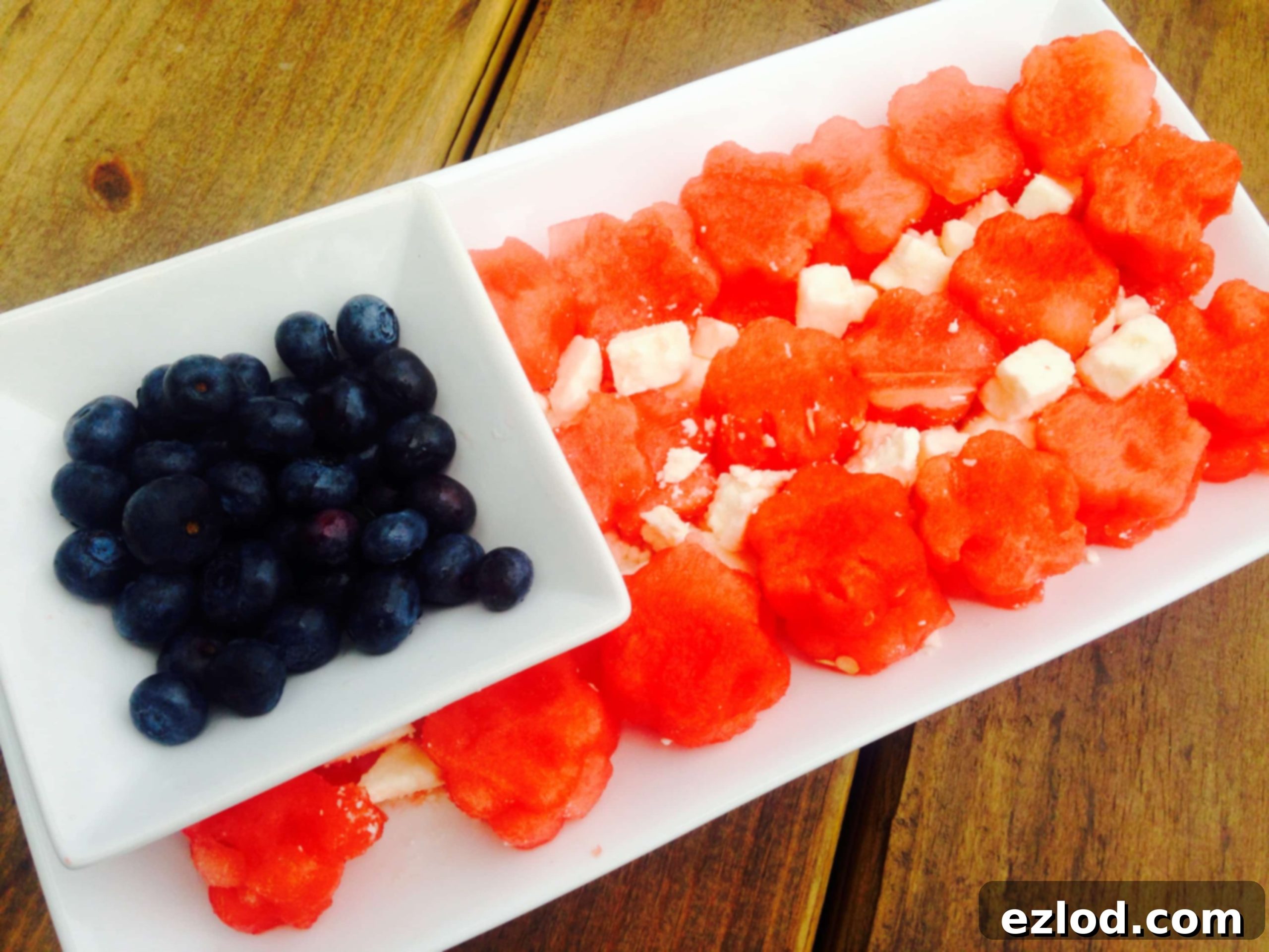 Watermelon, feta, and blueberries arranged in the shape of an American flag on a long rectangular serving plate with a wooden background