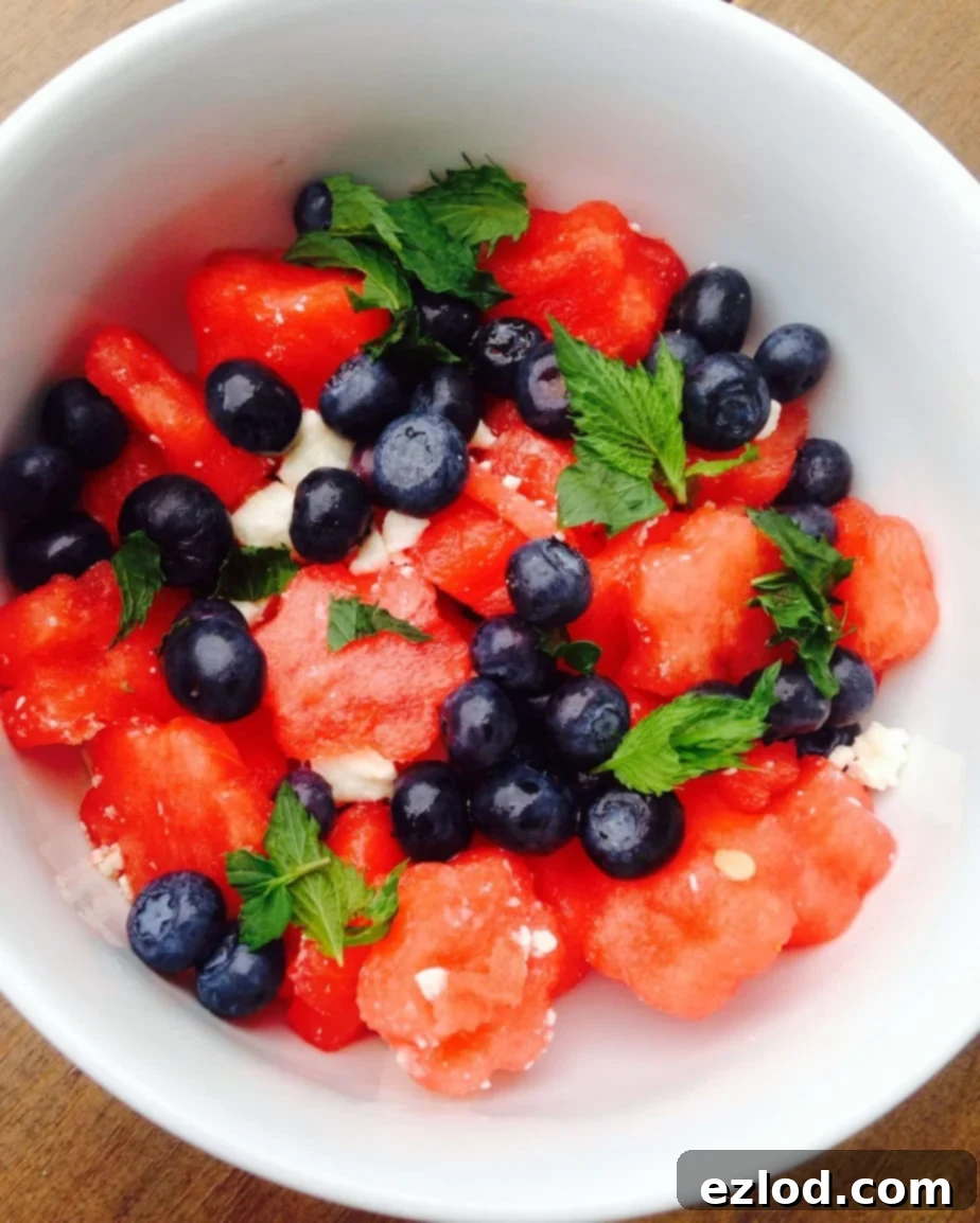 Watermelon, blueberries, feta, and mint mixed up in a white bowl, ready to serve