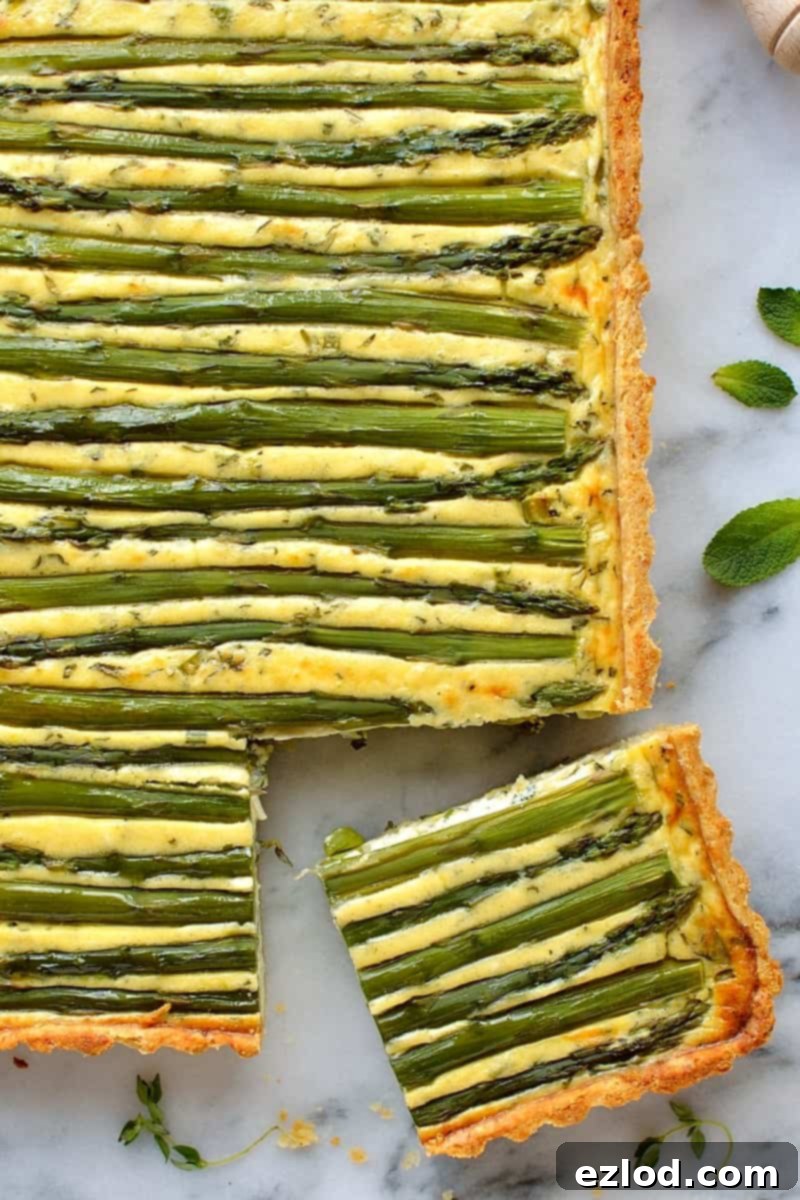 Overhead view of a rectangular asparagus, pea, and feta cheese tart (quiche) cooling on a wire rack, garnished with fresh herbs, ready to be sliced.