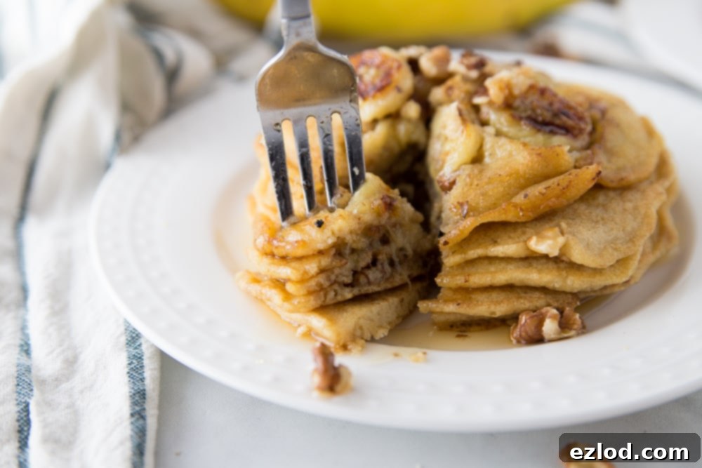 A stack of healthy 21 Day Fix banana pancakes topped with extra caramelized bananas, toasted walnuts, and a drizzle of maple syrup.