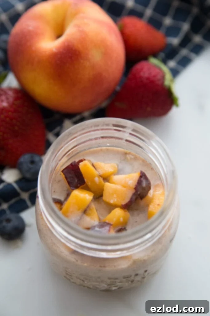 A jar of peaches and cream overnight oats sitting next to a large peach and some strawberries