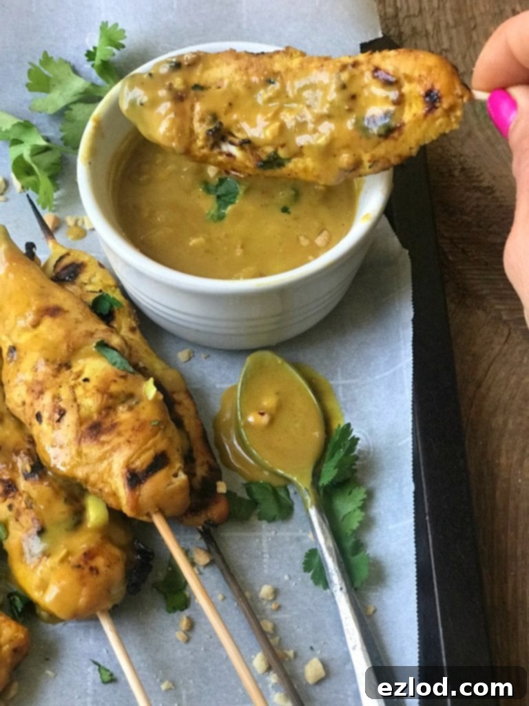 Chicken satay skewers with a bowl of creamy peanut sauce and fresh lime wedges, garnished with fresh cilantro.