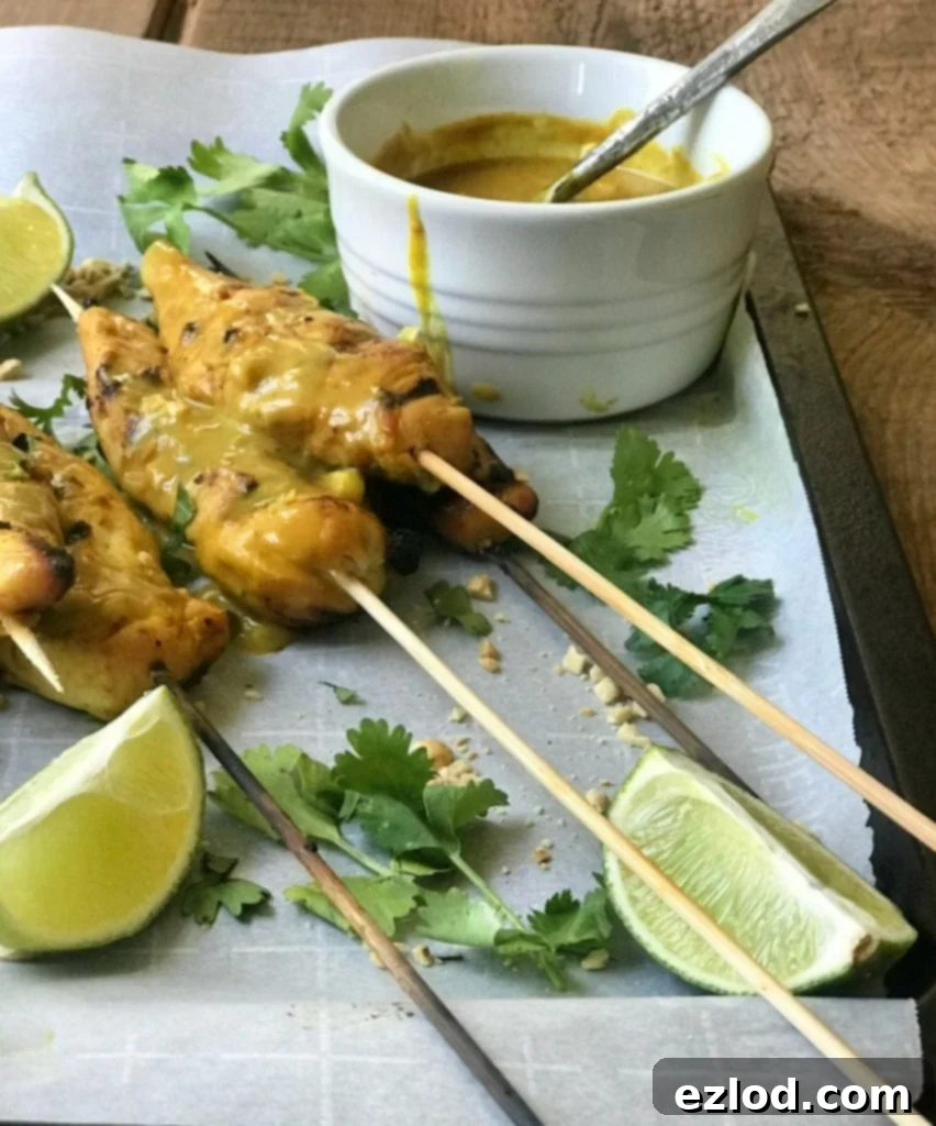 Hand dipping a chicken satay skewer into a bowl of rich, creamy peanut sauce.