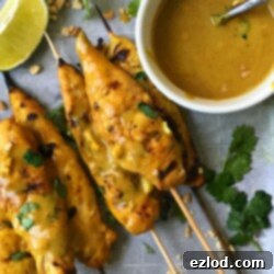 Chicken Satay Skewers on a Baking Pan with Creamy peanut sauce, crushed peanuts, and lime wedges