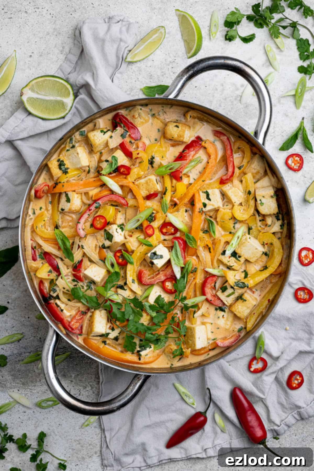 A pan of Thai style coconut tofu surrounded by herbs, lime slices and chillies.