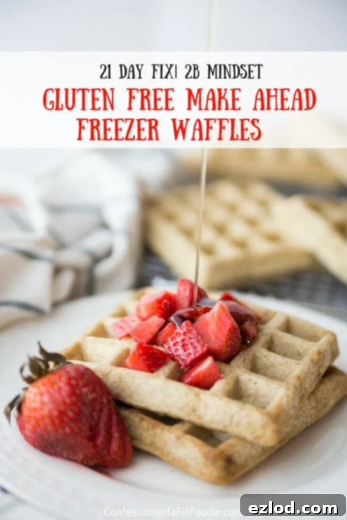 Two square homemade waffles on a white plate topped with diced strawberries and a sliced strawberry for garnish. Maple syrup is being drizzled from above. Has the text overlay- 21 Day Fix | 2B Mindset Gluten Free Make Ahead Freezer Waffles