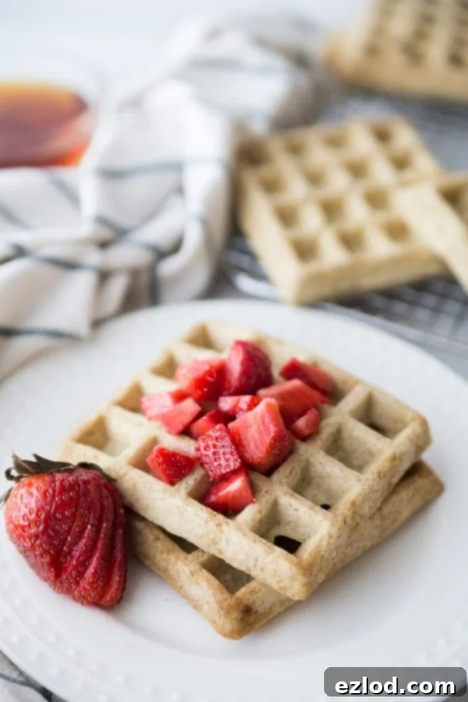 Two square homemade waffles on a white plate topped with diced strawberries and a sliced strawberry for garnish.