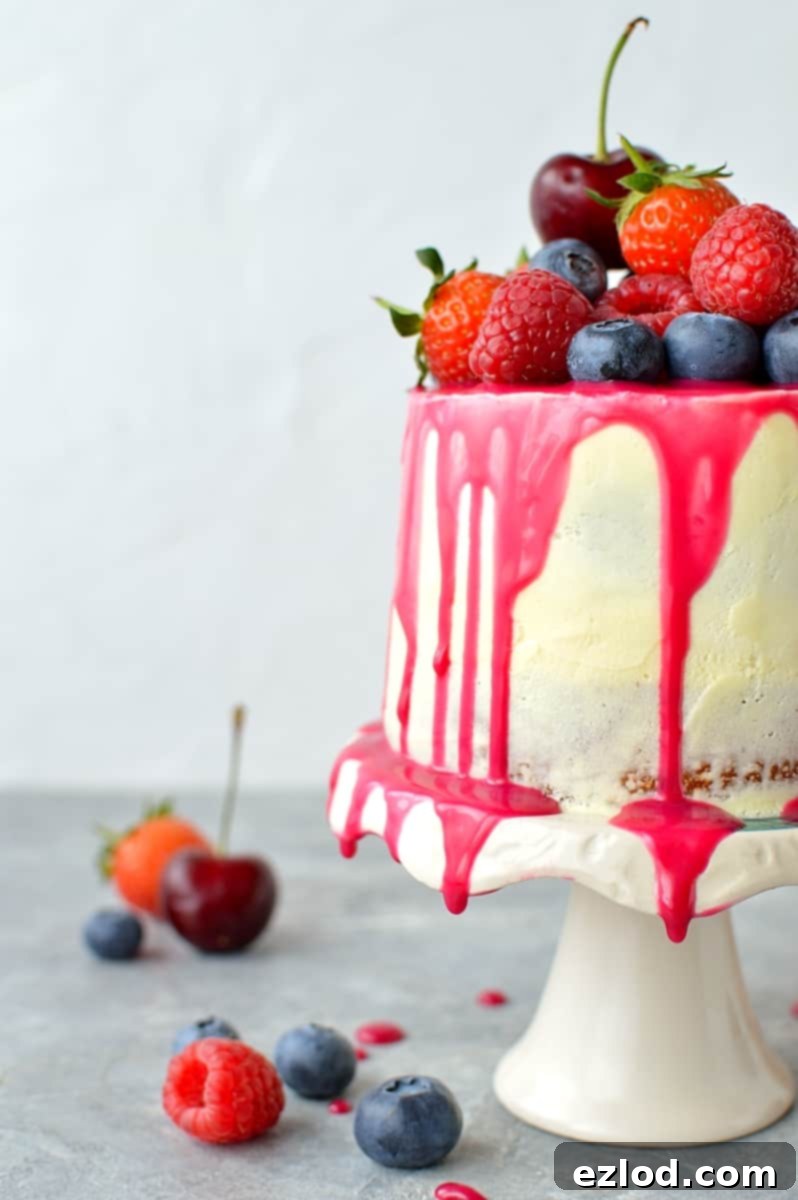 Mini white chocolate berry drip cake on a stand, showing the pink drip and fresh berries on top.