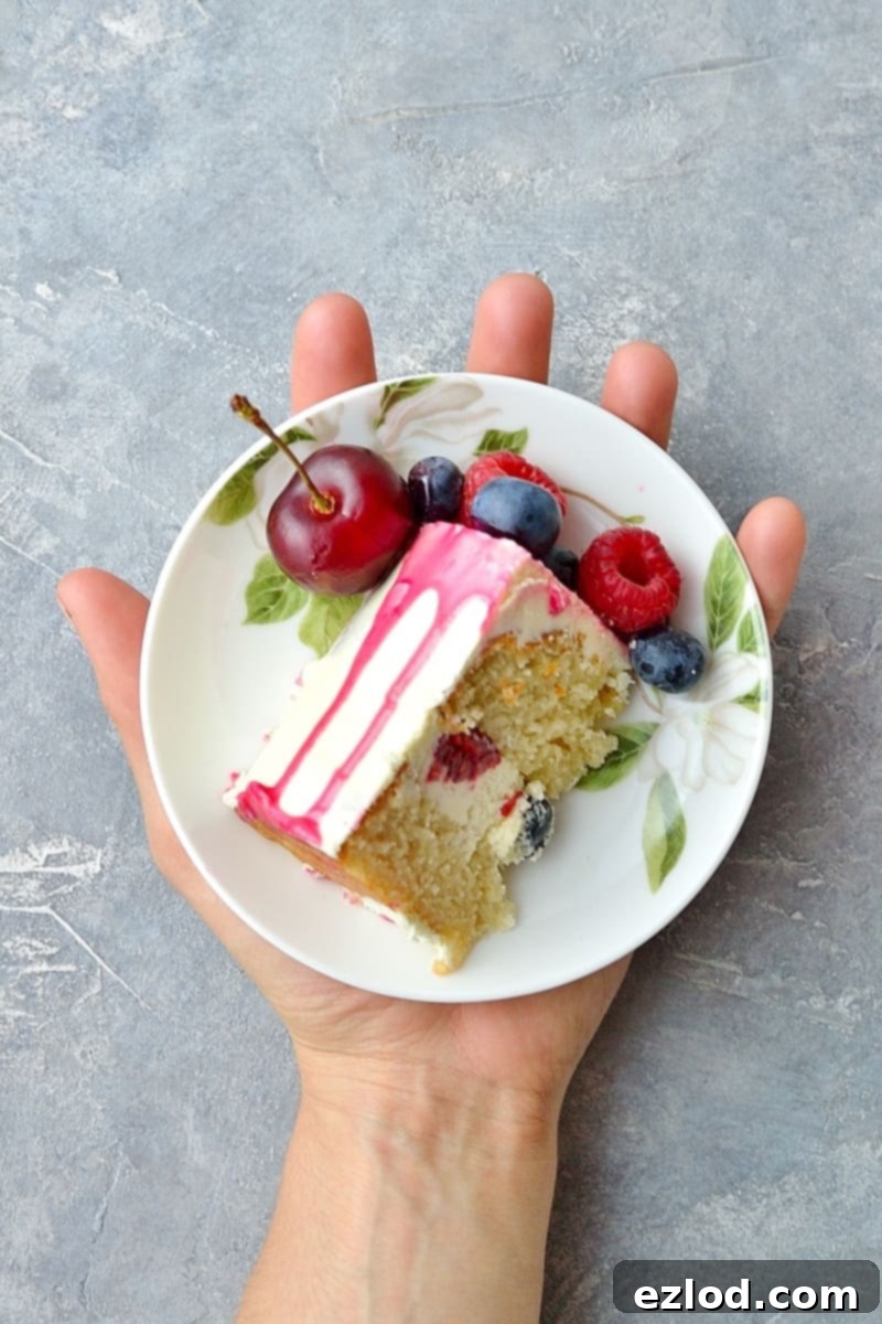 A close-up of a slice of mini white chocolate berry drip cake with a bite taken out, showing the layers of cake, ganache, and berries.