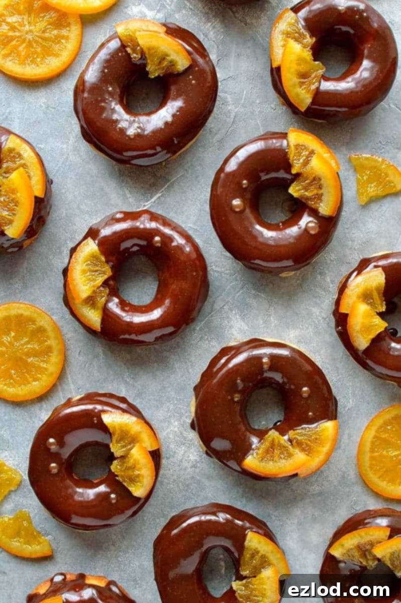 Three chocolate orange doughnuts on a white plate with one bitten, showing the soft interior.