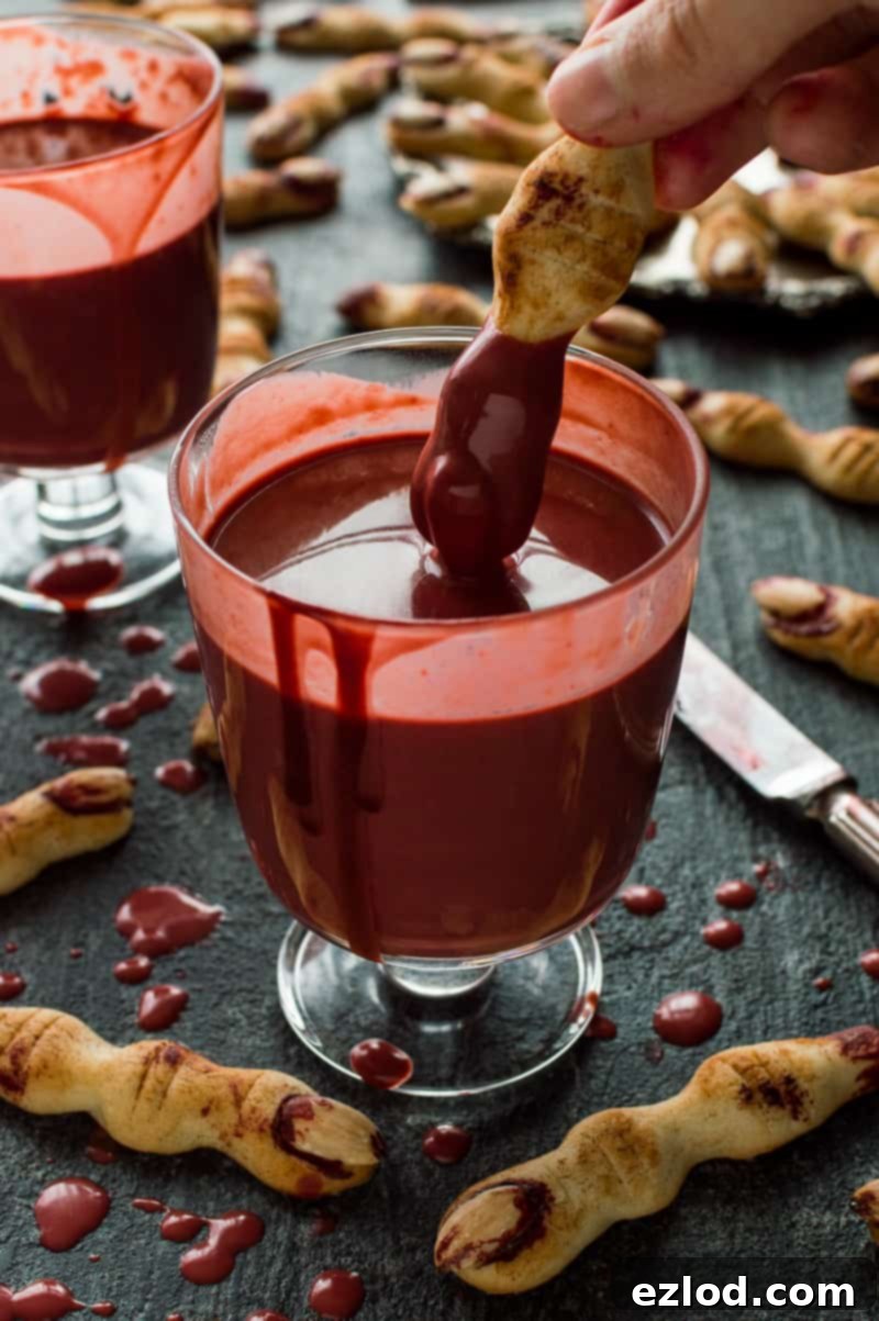 A witch finger shortbread cookie being dipped in a glass of red velvet hot chocolate.