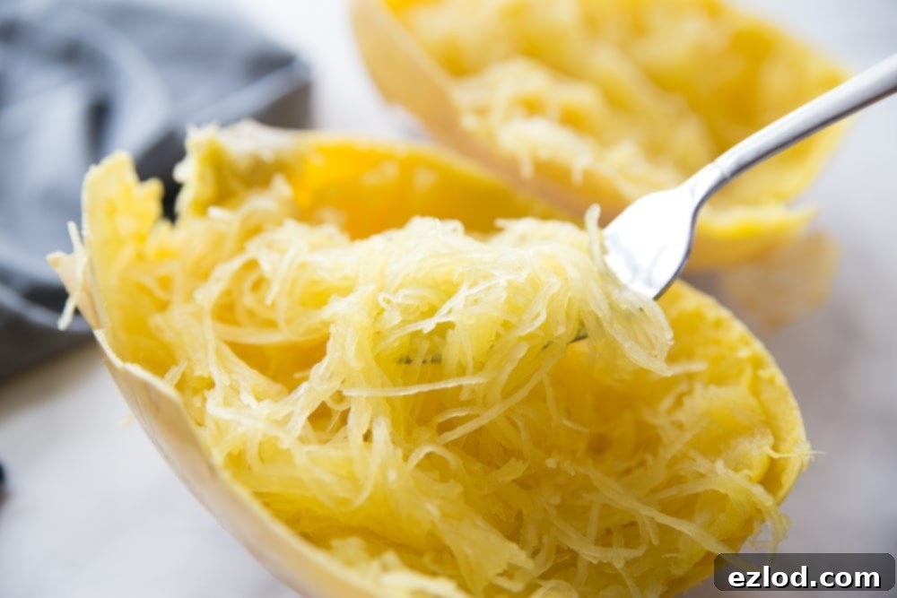 Cooked spaghetti squash half with squash strands on a fork, ready for a bite.