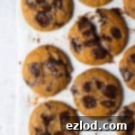 Vegan pumpkin chocolate chip cookies on a sheet of baking parchment on a grey backdrop.