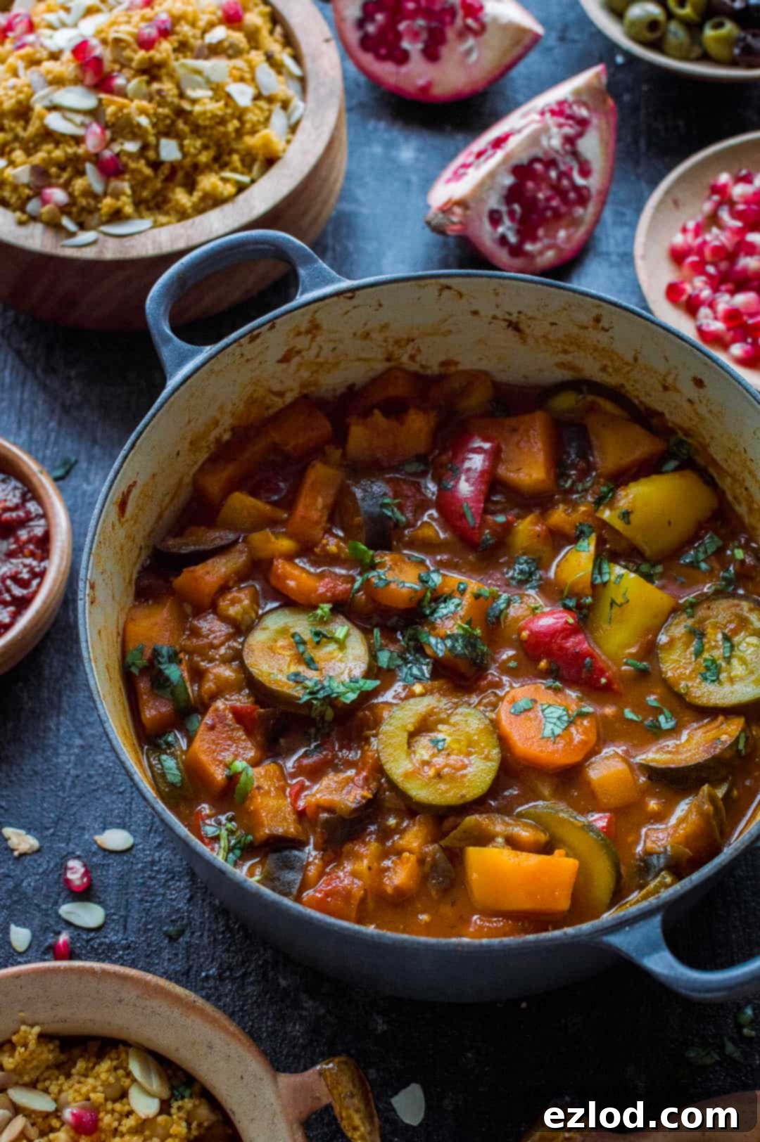 An inviting angled shot of a vegan vegetable tagine, brimming with tender aubergine, courgette, carrots, and bell peppers, presented in a rustic casserole dish with a side of light couscous and pomegranate seeds for garnish. Ideal for a healthy, comforting meal.