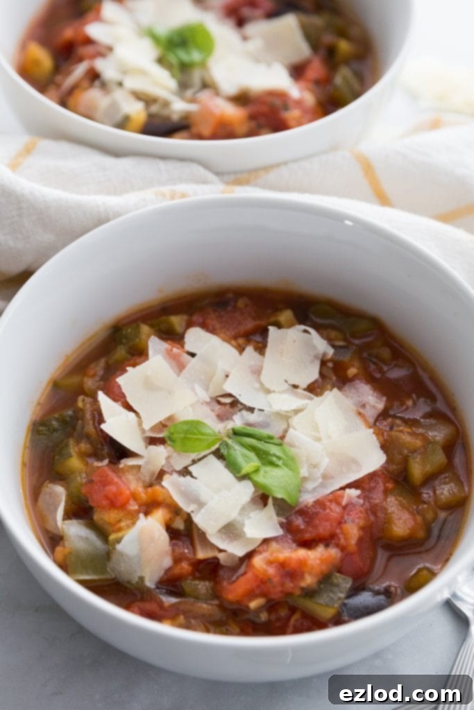 Two white bowls overflowing with vibrant Instant Pot Ratatouille, garnished with grated Parmesan cheese and fresh basil leaves, set against a rustic background.