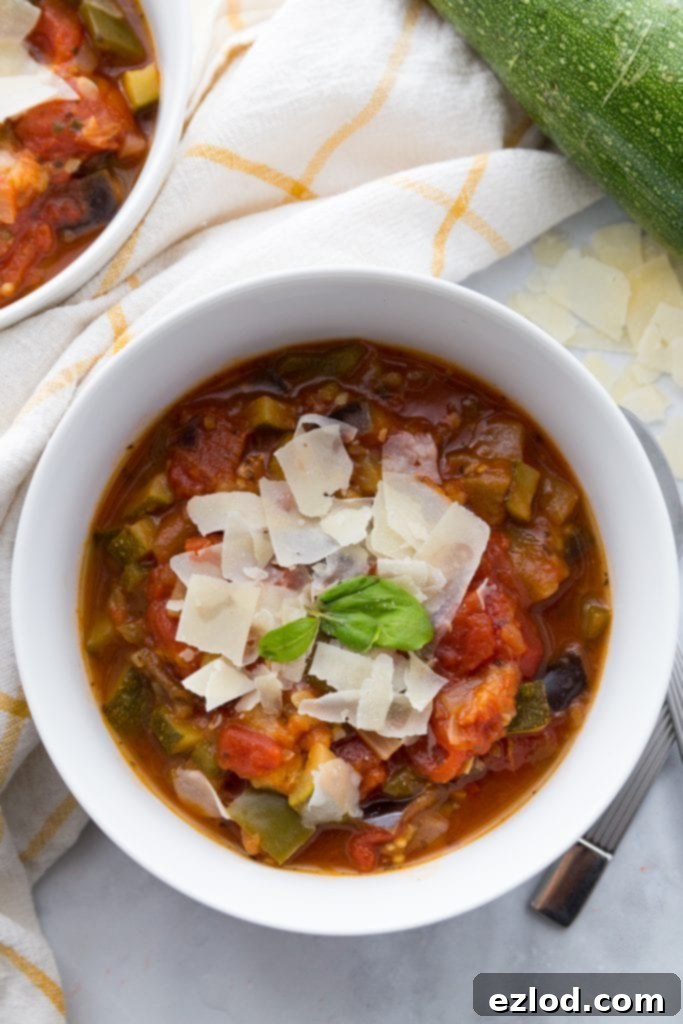 Two white bowls of Instant Pot Ratatouille, garnished with Parmesan and fresh basil, set on a white and yellow plaid towel, with a background of warm, inviting kitchen tones. The image evokes comfort and fresh ingredients.
