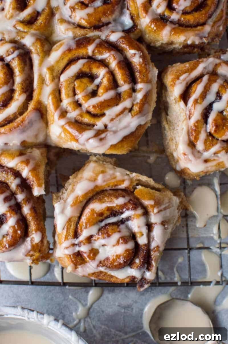 Vegan wholemeal maple cinnamon rolls cooling on a wire rack, with a tempting bowl of maple glaze beside them, ready to be drizzled.