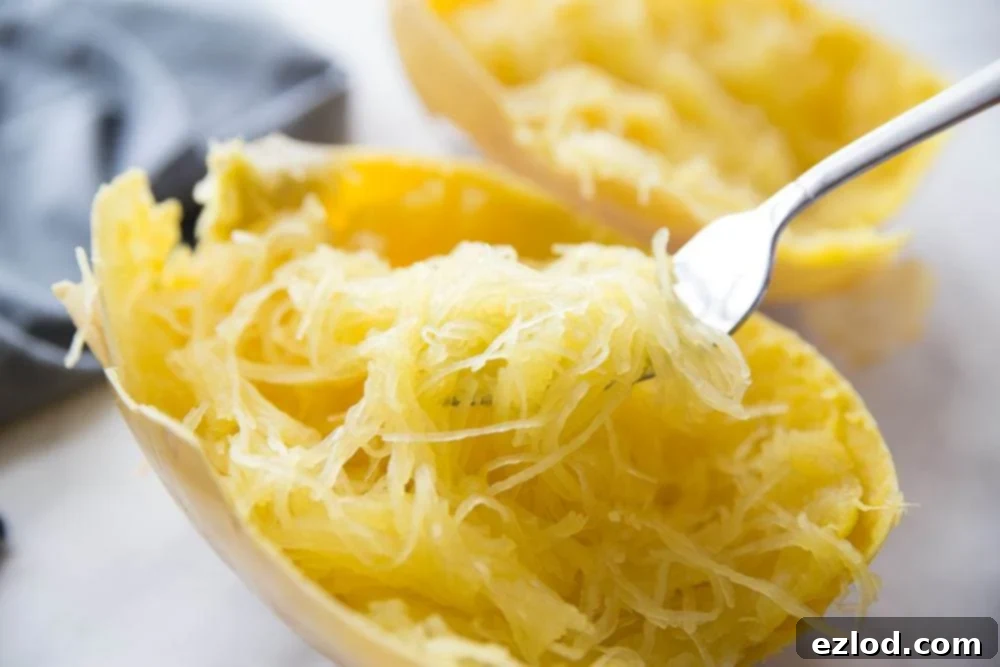 Cooked spaghetti squash cut in half with a fork showing the yellow strands of squash spaghetti on a white background, ready to be served as a healthy pasta alternative.