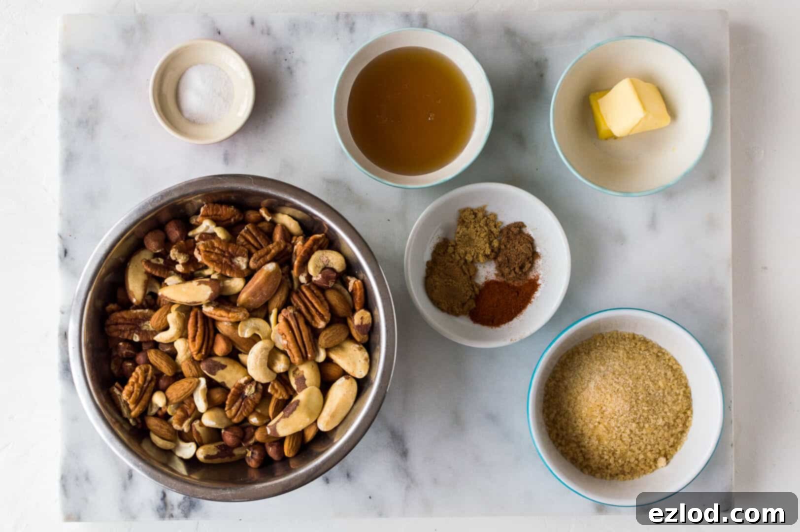 Essential ingredients for spiced honey roasted nuts, including mixed nuts, honey, butter, and various spices arranged on a surface.