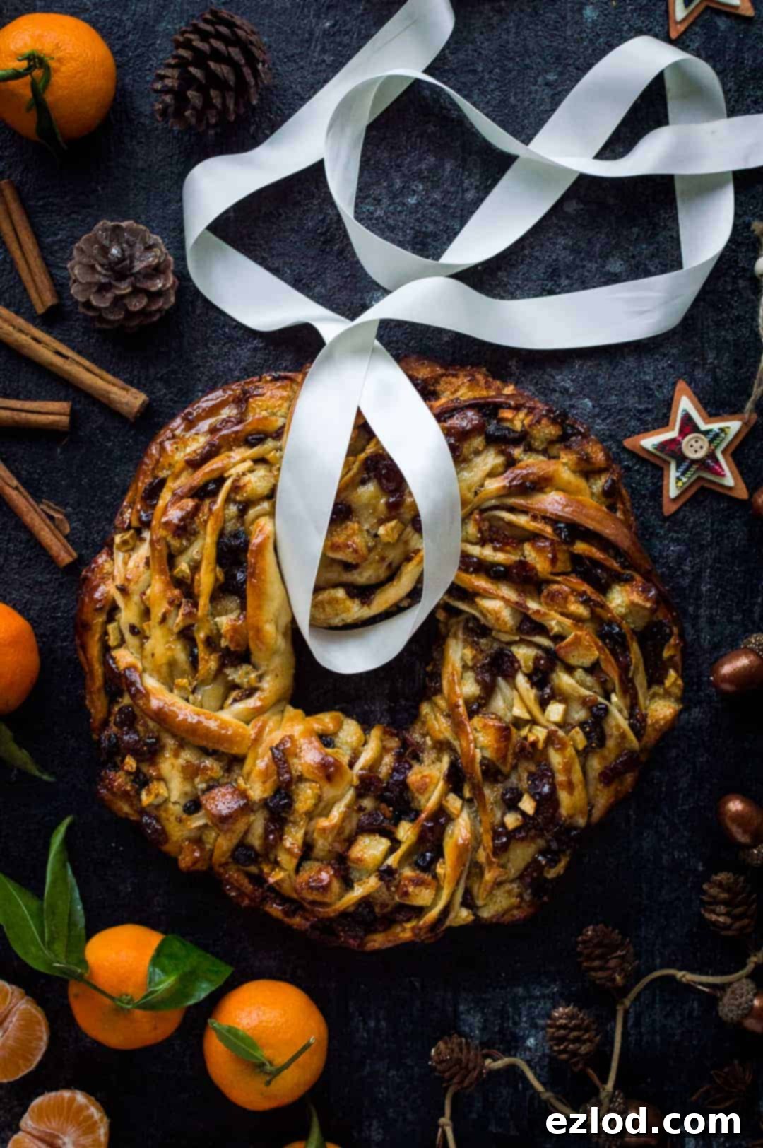 A top down shot of a braided bread wreath filled with fruit mince, marzipan and apple; surrounded by clementines, spices and Christmas decorations