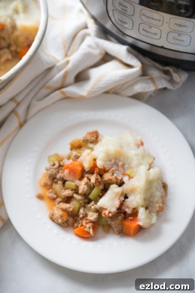 White plate with healthy shepherd's pie topped with mashed cauliflower and mashed potatoes sitting near an Instant Pot, showcasing a perfect portion of wholesome goodness.
