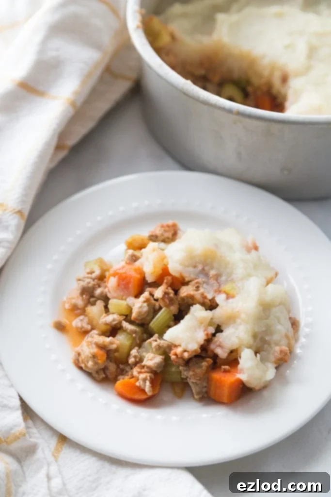 White plate with a generous serving of healthy shepherd's pie topped with a golden-brown mashed cauliflower and potato crust.