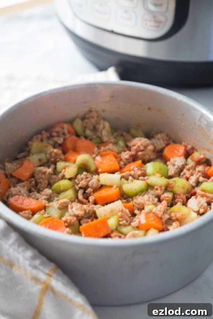 Instant Pot next to an aluminum insert containing seasoned ground turkey, carrots, and celery, ready for the pot-in-pot cooking method.