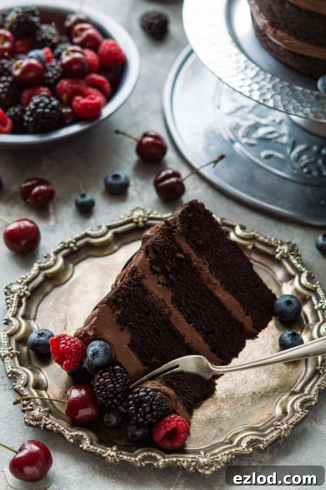 Slice of easy vegan chocolate cake with vegan ganache on a pewter platter with fresh berries.