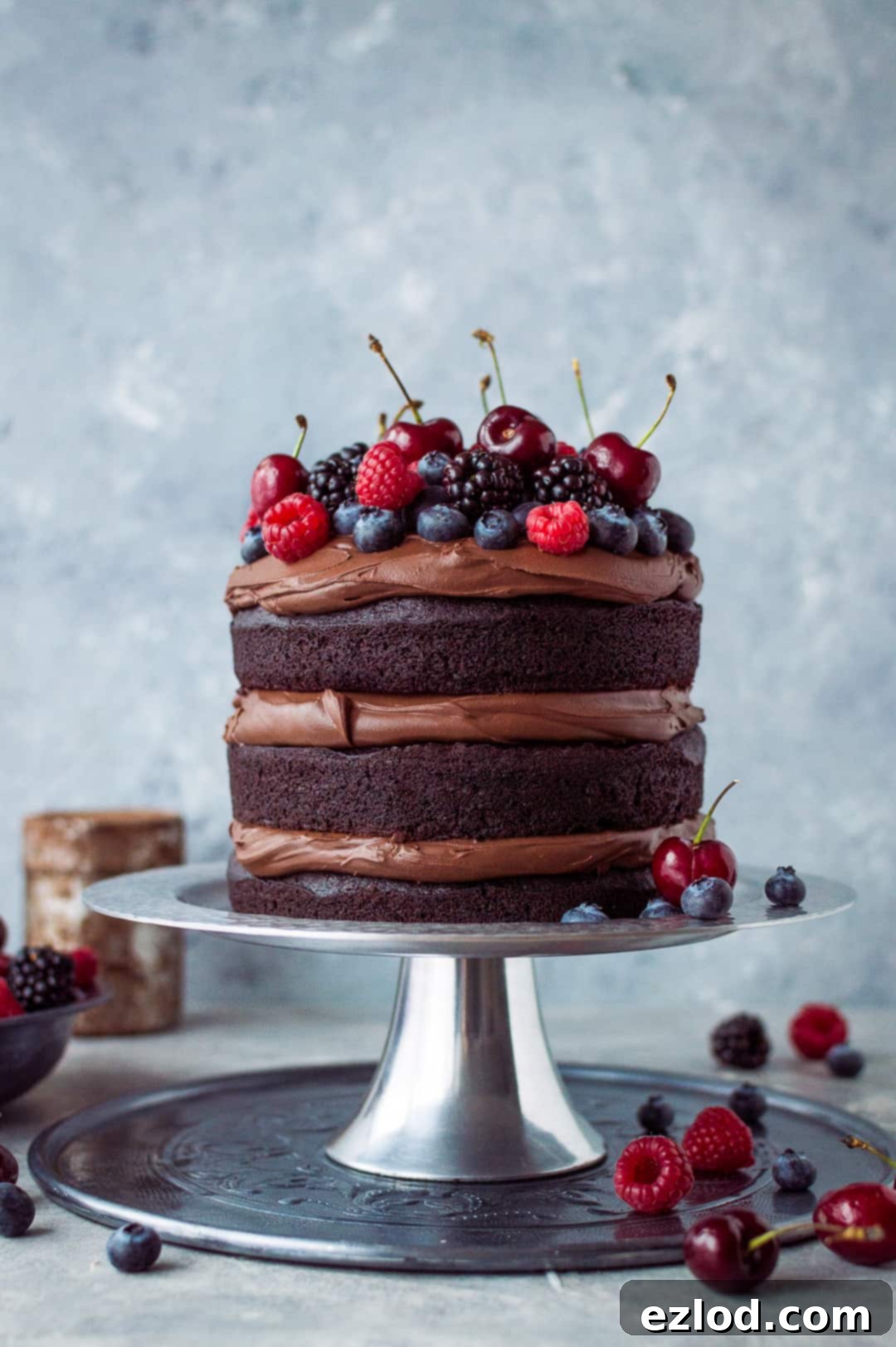Vegan chocolate fudge cake with coconut milk ganache and fresh berries on a silver cake stand.