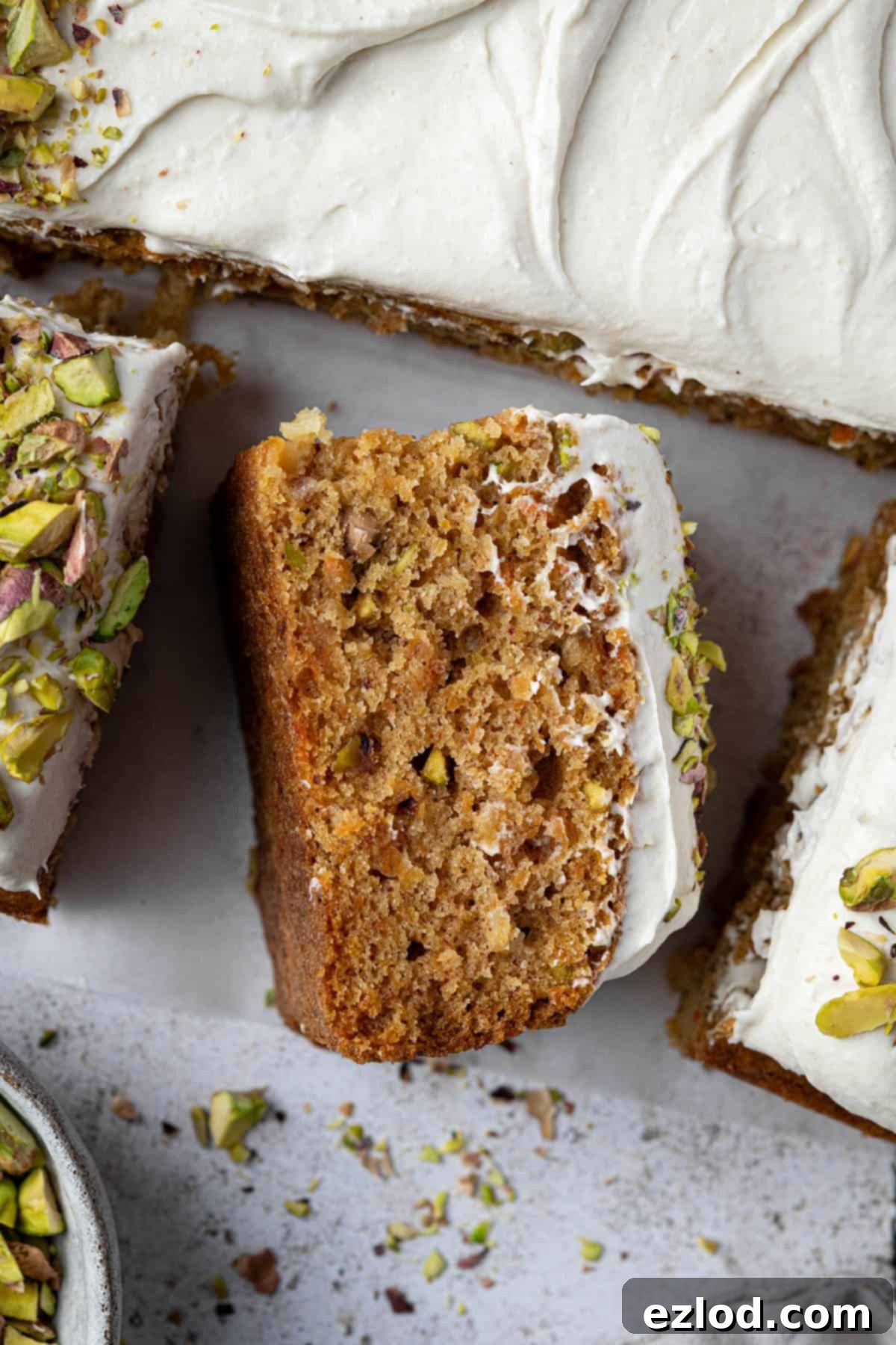 Close up of a moist slice of vegan carrot, pineapple and pistachio cake topped with creamy white chocolate frosting.