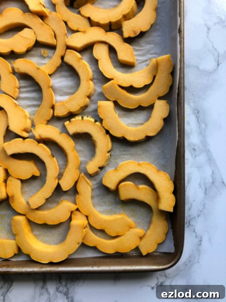 Sliced delicata squash on a rimmed baking sheet over parchment paper