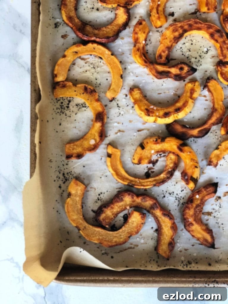 Roasted delicata squash on a baking sheet. Edges are crispy and the fries are seasoned. 