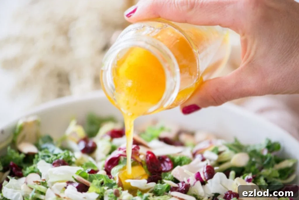 Close up of a woman's hand pouring maple cider vinaigrette out of a glass jar onto a bed of festive Holiday Salad.