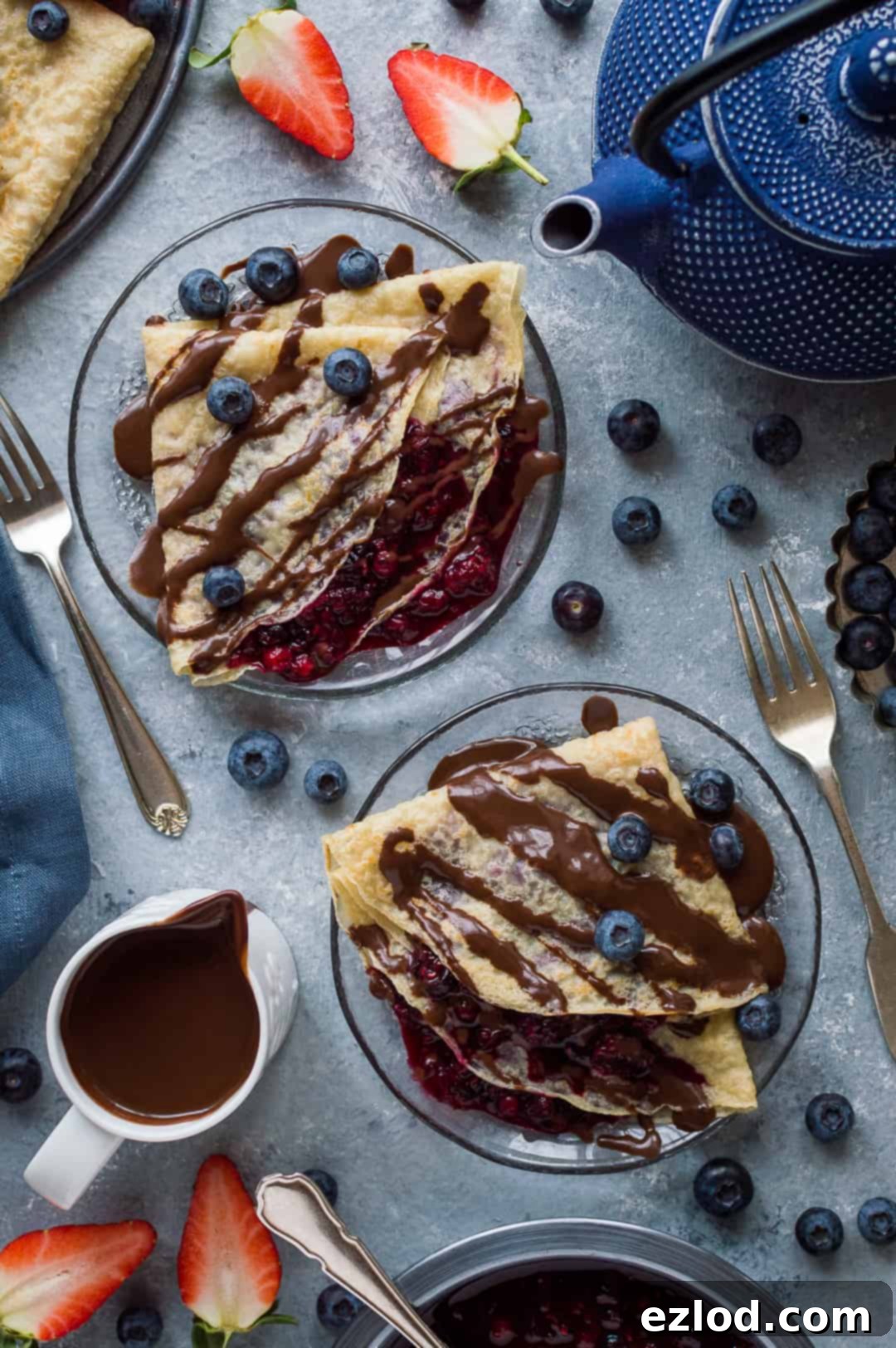 Vegan pancakes filled with mixed berry compote and topped with vegan chocolate sauce on glass plates.