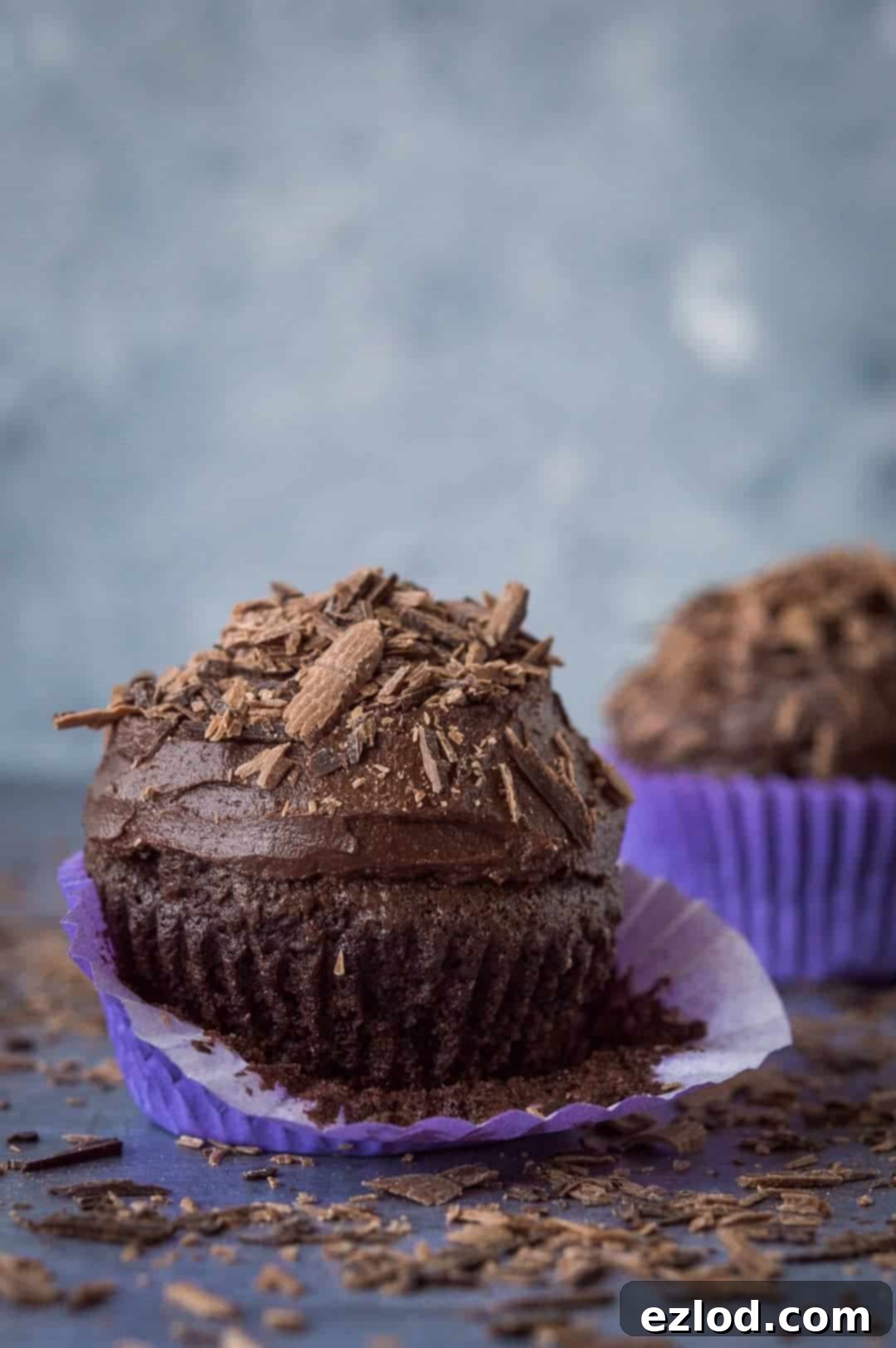 close up of a chocolate cupcake topped with buttercream and chocolate shavings with the wrapper peeled down, showcasing the rich texture.