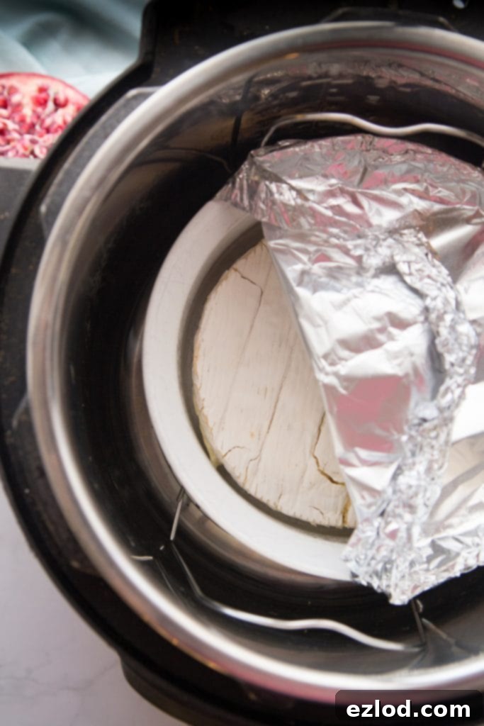 An Instant Pot with a white ceramic dish inside with a wheel of brie half covered in aluminum foil