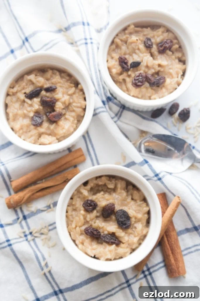 Three ramekins with healthy brown rice pudding, sitting on a blue and white cloth napkin. The rice pudding is topped with raisins and cinnamon, and cinnamon sticks sit nearby. 