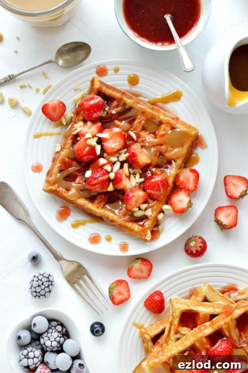 Peanut butter flavour square waffles topped with jam sauce, peanut butter sauce, strawberries and chopped peanuts.