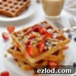 A stack of peanut butter and jelly waffles topped with strawberries and peanuts.