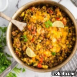 Overhead view of a colorful taco zucchini skillet in a pan, topped with melted cheese and sliced avocado, with lime wedges.