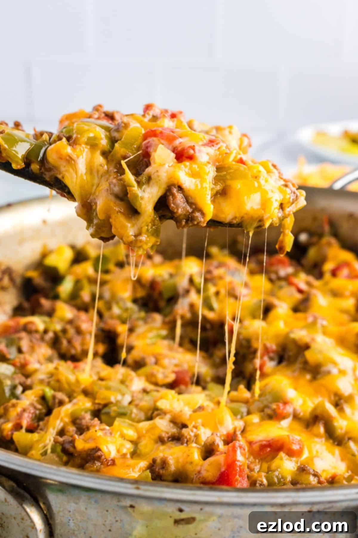 Close-up of a wooden spoon lifting a portion of gooey taco zucchini skillet with melted cheese and chunks of vegetables and meat.