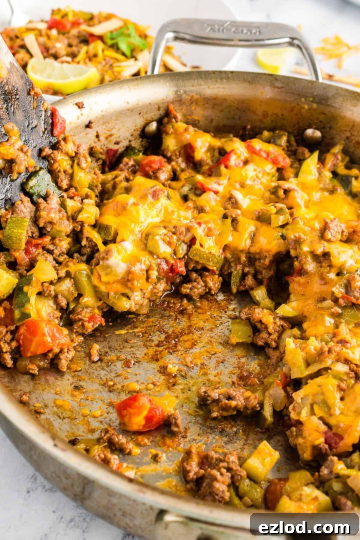 Partially eaten taco zucchini skillet in a pan, showing browned bits of meat and vegetables with a spatula partially visible.