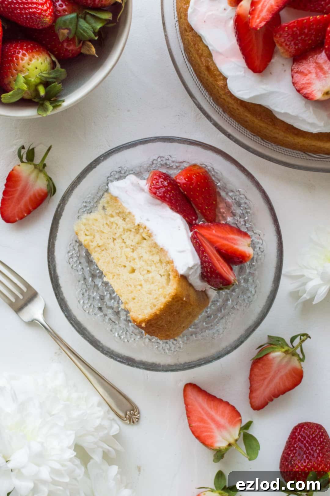 A top down shot of a slice of vegan lemon almond cake on a glass plate with strawberries