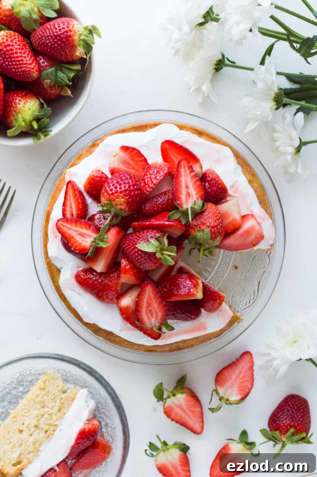 top down shot of vegan lemon almond cake topped with coconut cream and strawberries with a slice taken out.