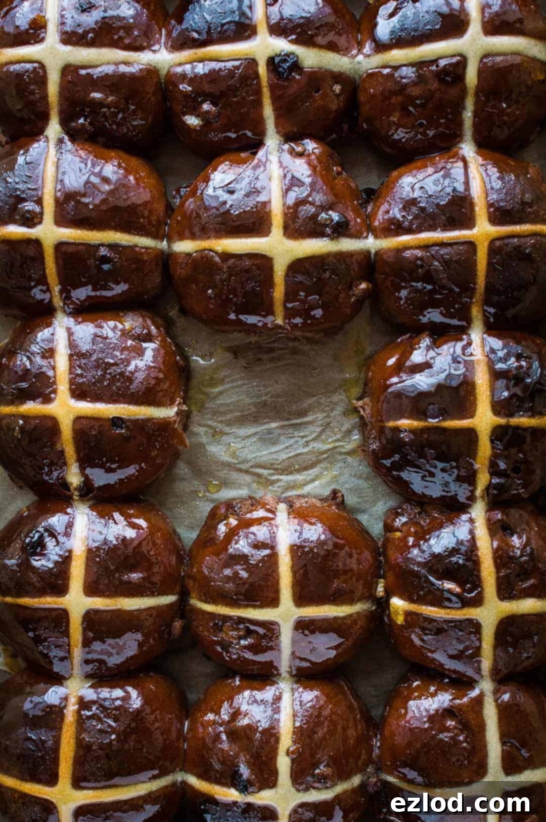 A top-down shot of freshly baked chocolate orange hot cross buns arranged on a white surface, with one bun removed from the center, revealing its soft interior.
