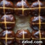 Close-up of freshly baked Chocolate Orange Hot Cross Buns, garnished with a glossy orange glaze and classic white crosses.