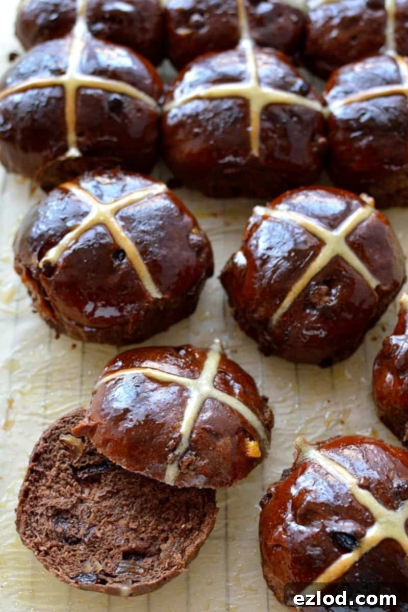 A close-up view of a freshly baked chocolate orange hot cross bun, sliced neatly in half to reveal its soft, chocolate-flecked interior and the vibrant orange zest throughout the dough.
